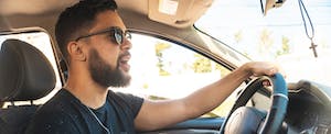 Young man wearing sunglasses driving his car and singing