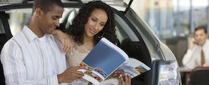 Man and woman reading brochure at car dealership