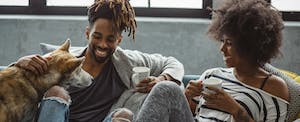 Young couple drinking coffee on sofa with their dog next to them
