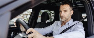 A man with a focused expression grasps the steering wheel while sitting in the driver's seat of his car.