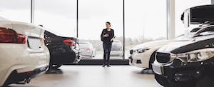 A woman stands in between rows of new cars in an auto dealership showroom.